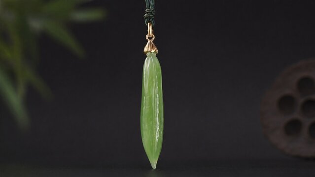 A slender green jade pendant shaped like a silique on a dark background.