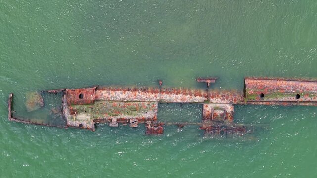 High-angle drone perspective looking down at the rusted metal hull of a historic WW1 German submarine wreck exposed at low tide.