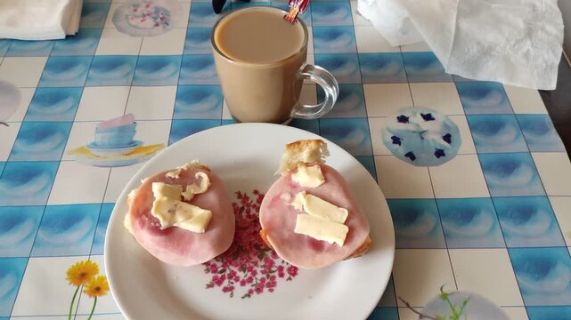 Breakfast plate with ham sandwiches and butter on patterned tablecloth with coffee mug