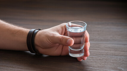 Shot of vodka, Man drinking alone, Bar counter background, Glass filled with alcohol, Depressed person at bar, Close-up of hand holding shot glass, Drunk man at pub, Clear strong alcohol © Jakub