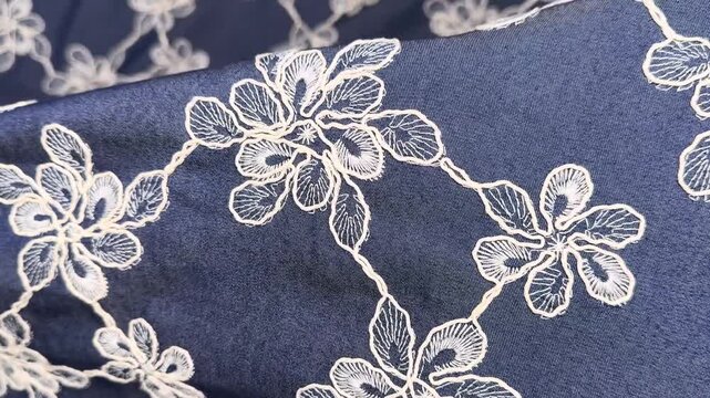 This premium navy blue fabric features delicate white floral embroidery and a scalloped edge detail providing a sophisticated look for custom apparel and refined fashion design projects