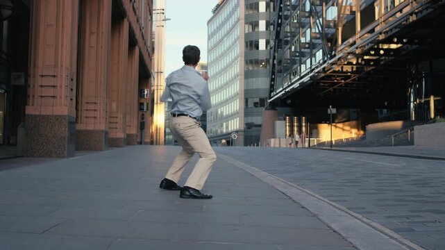 Excited businessman dancing in city street celebrating success and freedom during sunrise.