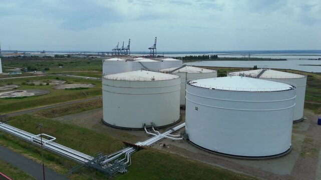 Aerial macro shot of liquefied natural gas storage tanks and complex industrial piping networks at an energy terminal.
