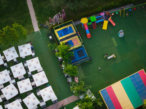 Aerial view of a vibrant children's playground featuring trampolines and colorful slides adjacent to an outdoor cafe area with white umbrellas in Tirane, Tirana County, Albania.