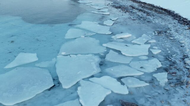 Aerial of large broken ice sheets along thawing Norway Arctic shoreline, drone