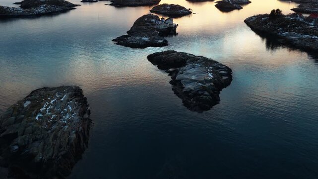 Rocky Arctic islets reflected in calm sunset waters near Lofoten Norway, drone