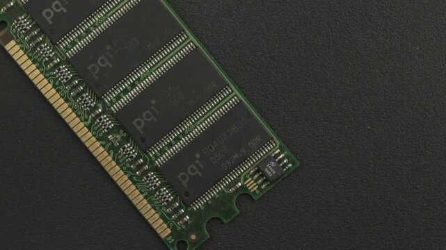 A green RAM module with visible circuitry details lies on a textured black surface. Ideal for tech tutorials or electronics presentations.