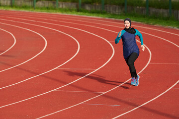 Fototapeta premium Female Athlete Wearing Hijab Running on Red Outdoor Track During Training Session