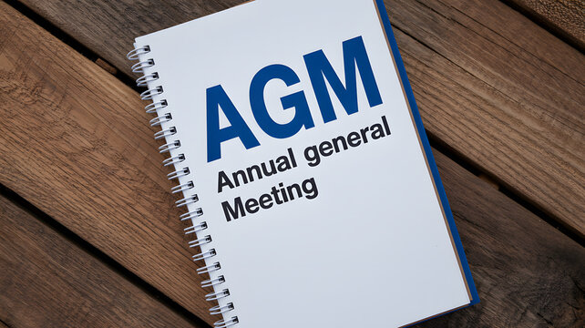A spiral bound notebook with AGM Annual general Meeting text on a wooden table