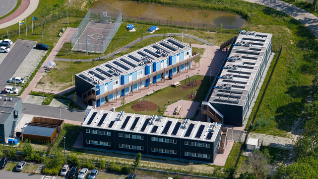 Aerial view of the KaFra Zevenbergen modular housing complex featuring solar panels on rooftops, a basketball court, and a playground in Zevenbergen, Noord-Brabant, Netherlands.