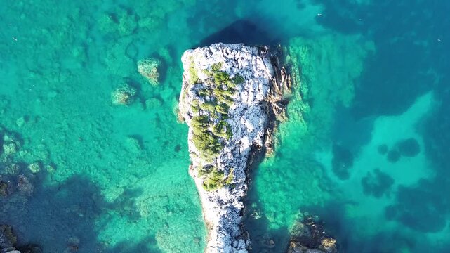 Aerial top-down view of a tiny isolated rock islet surrounded by clear ocean water