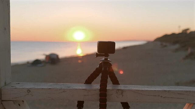 Professional camera setup recording colorful sunset on sandy beach coastline