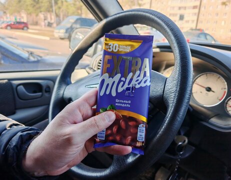 Belarus, Svetlogorsk, March 21, 2026. Person holding Milka Extra almond milk chocolate bar inside a car. Snack on the road, sweet food and daily life concept.