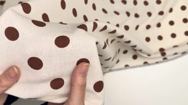 The soft linen and viscose material features a classic brown polka dot print on a cream base making it suitable for versatile clothing items like dresses and suits