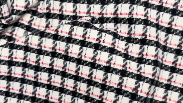 Woven woolen fabric featuring a classic check pattern in black, white, and subtle red lines, presenting a textured surface ideal for tailored outerwear and winter garments.
