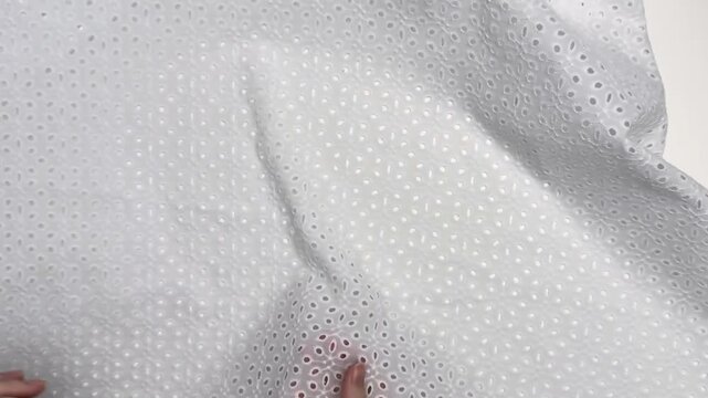 White cotton eyelet fabric featuring decorative cutout embroidery, showcasing a breathable and lightweight texture suitable for stylish summer apparel and children clothing.