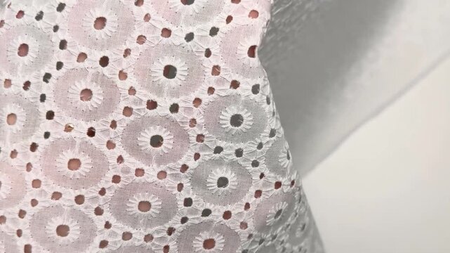 Close up of a lightweight white cotton eyelet textile featuring delicate circular embroidery patterns held by hands to demonstrate texture and transparency for summer apparel.