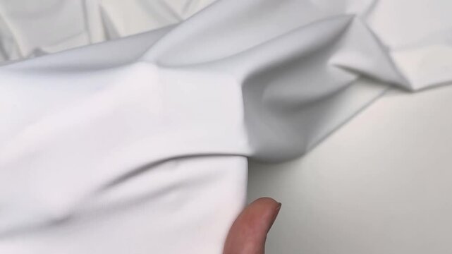 Close up of smooth white sport elastane fabric featuring high elasticity and matte surface texture held by hands to demonstrate stretchability and soft drape.