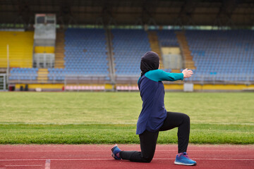 Obraz premium Muslim Woman in Hijab Doing Stretching Exercise on Running Track at Empty Stadium