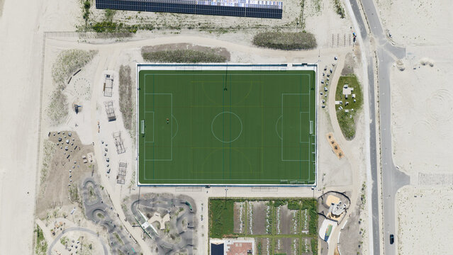 Aerial view of Sportpark Strandeiland featuring a green sports field surrounded by sandy terrain and a pump track in Amsterdam, North Holland, Netherlands.