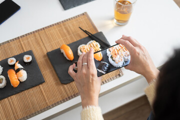 Person Eating Assorted Sushi with Chopsticks at Home © chandlervid85