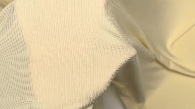 Close up of a soft pale yellow textile featuring a distinct ribbed texture displaying high elasticity and smooth draping qualities while resting on a flat surface.