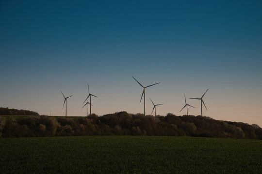 Wind turbines as silhouettes on a hill at twilight.
