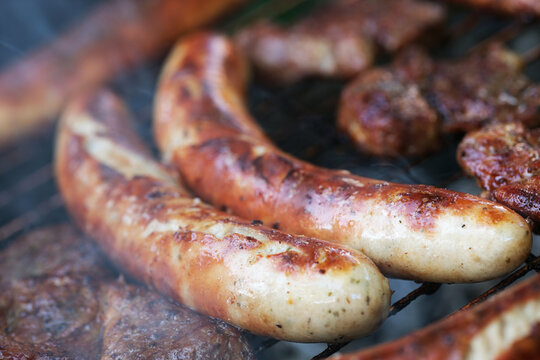 Zubereitung von Bratwurst und Schweinefleisch auf einem Holzkohlegrill.