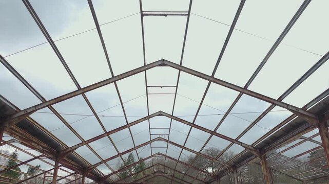 Symmetrical steel truss pattern inside deserted hangar with exposed skeleton and cloudy sky. Interior perspective focusing on geometric roof lines rust textures and empty industrial space. Post
