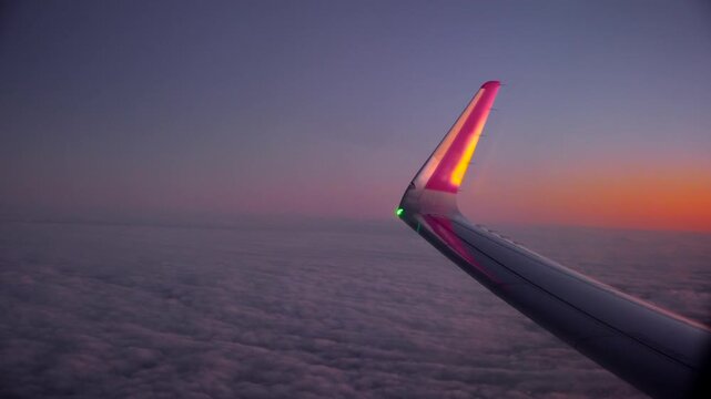 Aircraft cruising above cloud layer at sunset with glowing wingtip view. Window perspective revealing soft horizon gradient and endless cloudscape. Air travel journey, aviation transport, calm sky