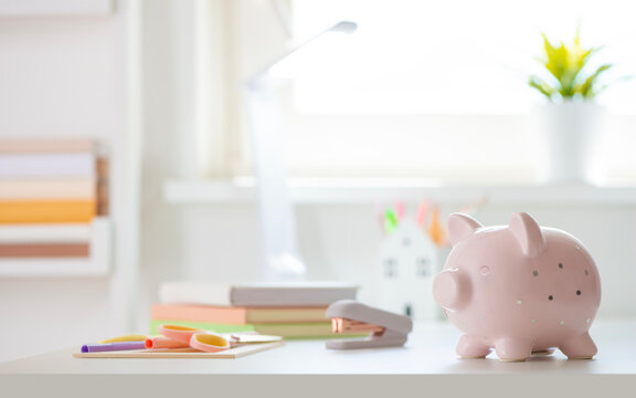 Education concept with pink piggy bank on table with various stationery and blurred classroom background