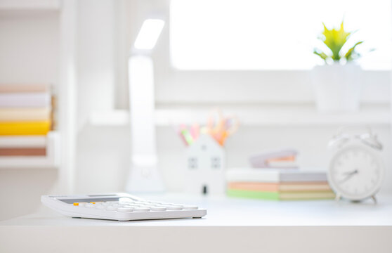 White calculator on educational table top with blurred background of student room interior with book shelf and window