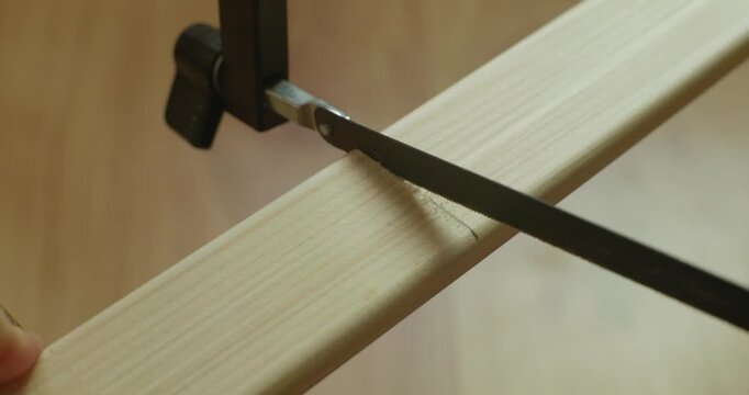 Close up view of sawing a wooden lath with a hacksaw blade while a hand holds it in place