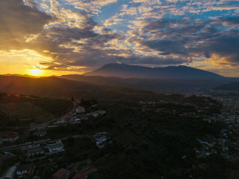 Aerial view of the rolling hills and city of Berat with Mount Tomorr in the background under a dramatic sunset sky Berat, Qarku i Beratit, Albania.