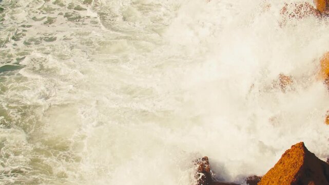 Ocean Waves at high tide roll in and crash against the coastal cliffs, huge rocks. Crashing waves creating huge splashes.   Top view of the coastal cliffs with large waves crashing against the rocks