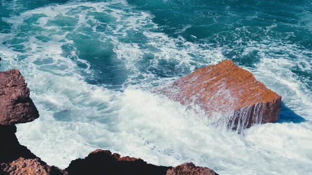 Waves at high tide roll in and crash against the coastal cliffs, huge rocks. Close-up of crashing ocean waves creating huge splashes.