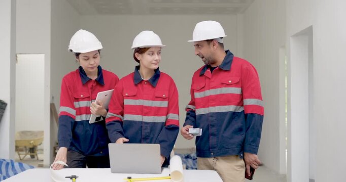 Asian female engineer leads building site discussion with inspector and contractor, checking ceiling work, blueprint details, safety compliance, renovation progress, and quality issue indoors.