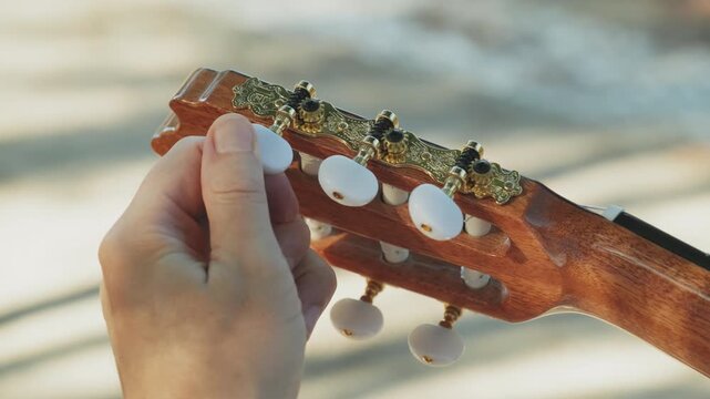 Guitarist adjusts the guitar by twisting the pegs - close-up. Guitar tuning process. The musician's hands twist beautiful white pegs on the guitar's head.  Beautiful golden guitar pegs