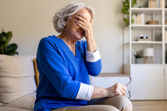 Senior woman suffering from headache or migraine is covering her face with hand