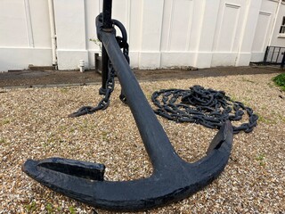 Massive historic black metal ship anchor resting on the ground © Curiosity Photos