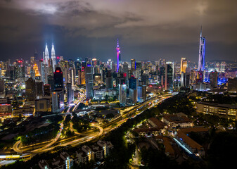 Fototapeta premium Aerial night view of Kuala Lumpur featuring illuminated skyscrapers, colorful city lights and highway light trails. Urban skyline showing modern city life in Malaysia.