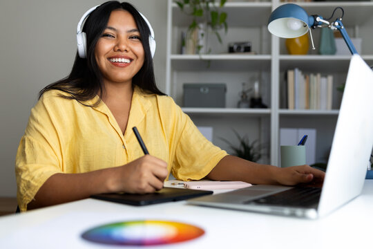 Latin graphic designer working from home using laptop and drawing tablet