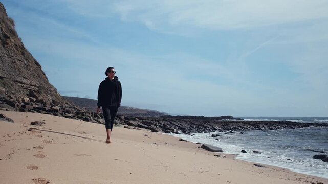 On a hot summer day, a young man wanders barefoot on an empty sandy beach.  On a beautiful day, a man walks along a sandy beach.  A man in an amorous mood on the beach, admiring nature's beauty.