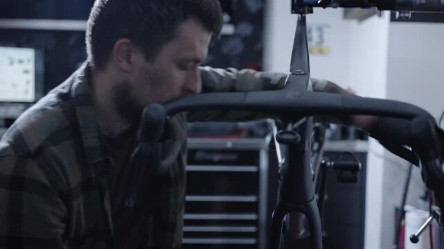 Focused male mechanic fixing expensive black carbon road bike in specialized workshop. Technical service of high-end racing bicycle cockpit, integrated handlebar tuning and precise maintenance.