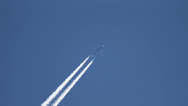 Airplane cruising overhead with long symmetrical vapor trails in cloudless sky, navigation and global transport theme. Linear contrail pattern representing carbon output and atmospheric change