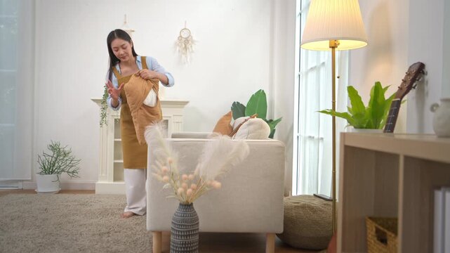 Young Asian woman dusting and cleaning furniture in a cozy modern living room
