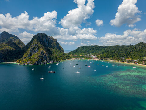 Aerial drone view of Corong Corong Bay in El Nido, Palawan, Philippines with turquoise sea, tropical mountains, anchored boats, and moving clouds above the coastline.