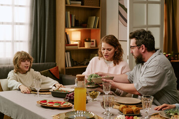 Medium shot of Caucasian family of three eating Sunday lunch, together and sharing conversation, showing family bonding and weekend routine. Useful for parenting, home life marketing