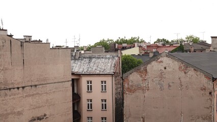 Widok na zwartą, wielkomiejską zabudowę starych kamienic z widocznymi odrapanymi ścianami szczytowymi. W tle widać dachy budynków, klasyczne okna oraz kępę zielonych drzew pod jasnym niebem. © tomo81