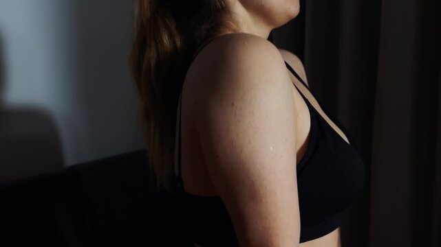Woman's upper body wearing a black sports bra, captured from a side perspective with natural light, emphasizing natural curves and healthy skin texture, portraying body confidence and wellness